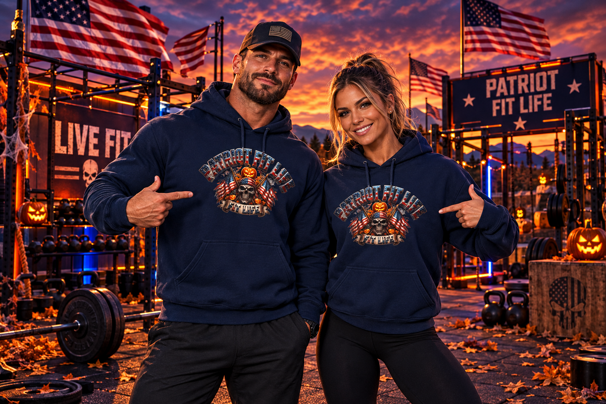 A man and a woman pose together in a gym at sunset wearing matching navy blue hoodies with a patriotic Halloween graphic print that reads 'PATRIOT FIT LIFE.' The background shows American flags, workout equipment, and Halloween decorations.