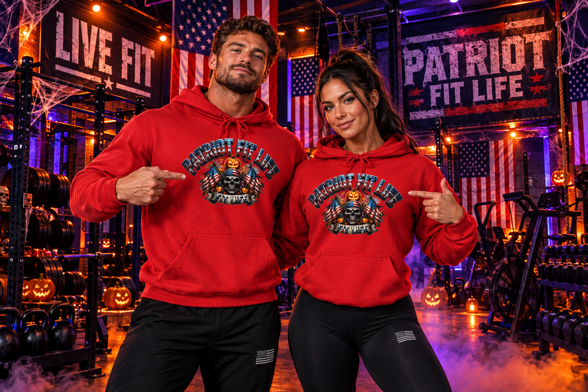 A man and a woman pose together in a gym setting, both wearing matching red hoodies with a graphic print that reads 'PATRIOT FIT LIFE.' The background features patriotic and Halloween-themed decor, including American flags, 'LIVE FIT' and 'PATRIOT FIT LIFE' signs, and jack-o'-lanterns.