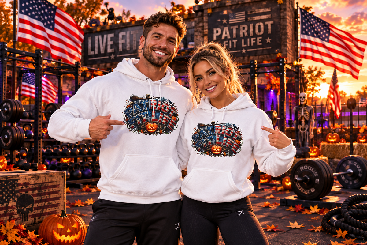 A man and a woman pose in a gym wearing matching white hoodies with a colorful Halloween patriotic PATRIOT FIT LIFE graphic design featuring a jack-o'-lantern's and American flags. The background features a rustic gym setting with autumn decorations, pumpkins, and American flags.