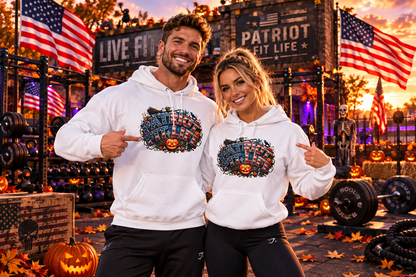 A man and a woman pose in a gym wearing matching white hoodies with a colorful Halloween patriotic PATRIOT FIT LIFE graphic design featuring a jack-o'-lantern's and American flags. The background features a rustic gym setting with autumn decorations, pumpkins, and American flags.