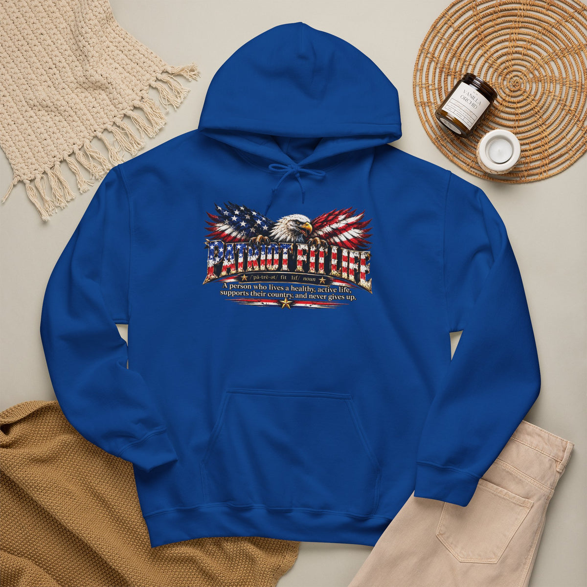 A royal blue pullover hoodie laid flat on a light beige surface, featuring a PATRIOT FIT LIFE dictionary-style definition graphic across the chest. 