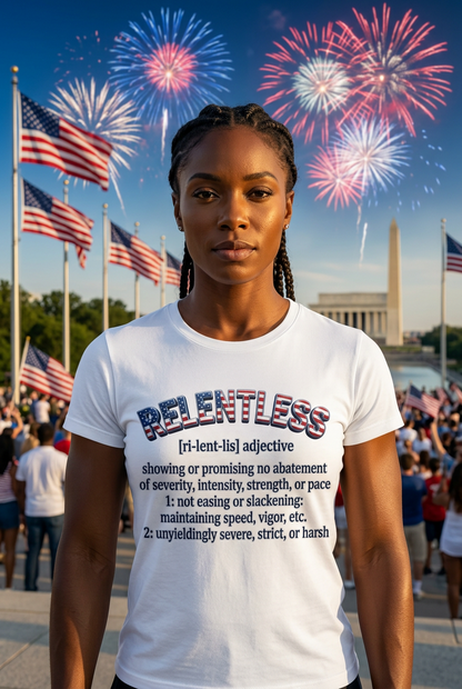 A woman stands outdoors in front of fireworks and the Washington Monument, wearing a white graphic T-shirt with a RELENTLESS dictionary-style definition printed on the front.