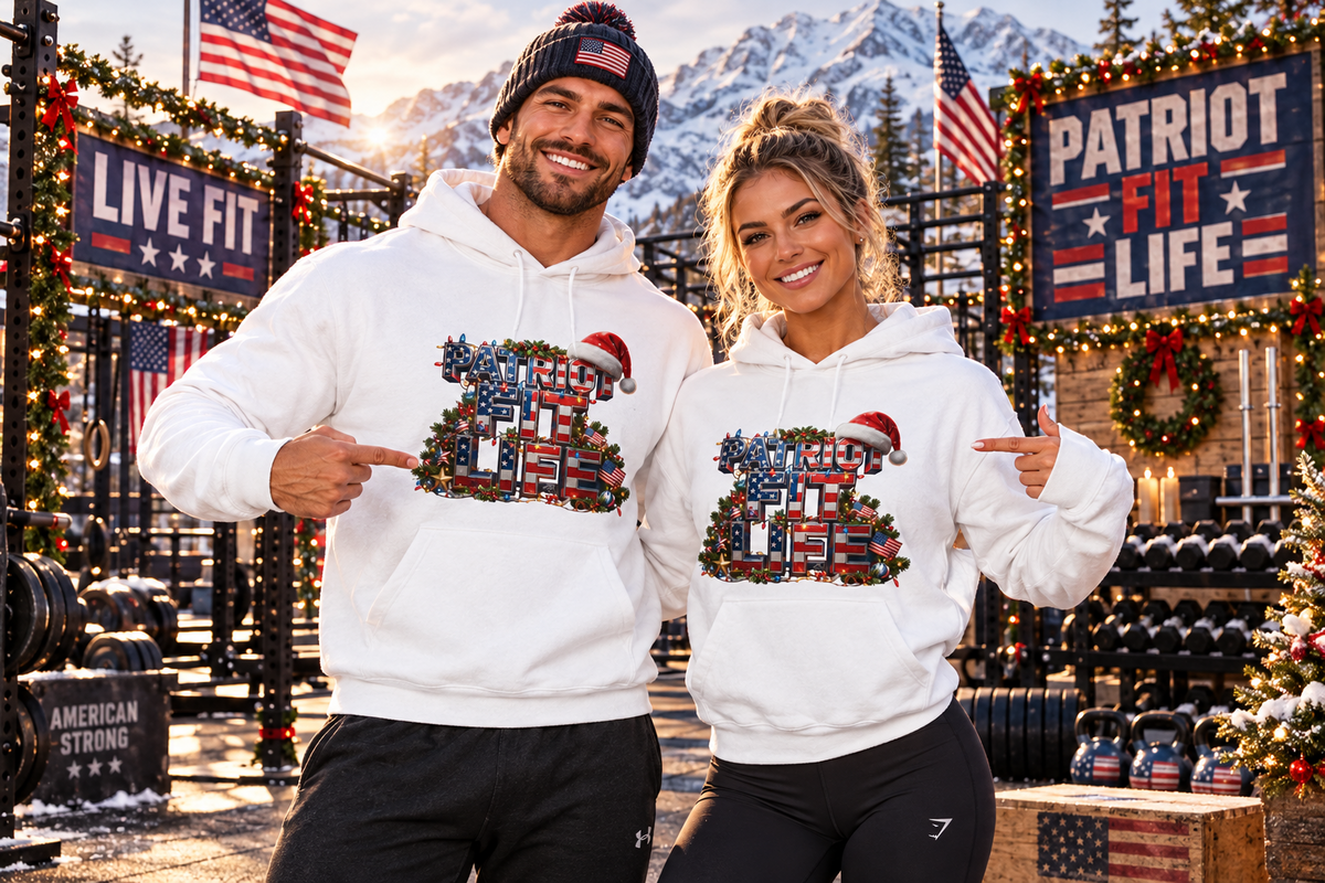 A man and a woman stand in a decorated fitness gym wearing matching white hoodies with a patriotic Christmas-themed graphic. The graphic features a decorated Christmas tree with American flags, the words 'PATRIOT FIT LIFE,' and a Santa hat.
