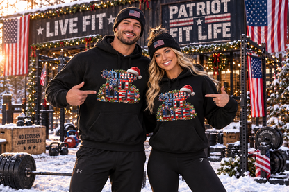 A man and a woman posing together in a snowy outdoor gym setting, both wearing matching black hoodies with a colorful patriotic Christmas graphic on the front and black beanie hats with American flags.