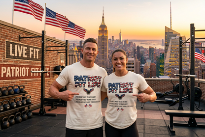 A man and a woman stand on a rooftop gym overlooking a city skyline at sunset, wearing matching white T-shirts with a patriotic 'Patriot Fit Life' graphic. The background includes American flags, weight racks, kettlebells, and the Empire State Building.