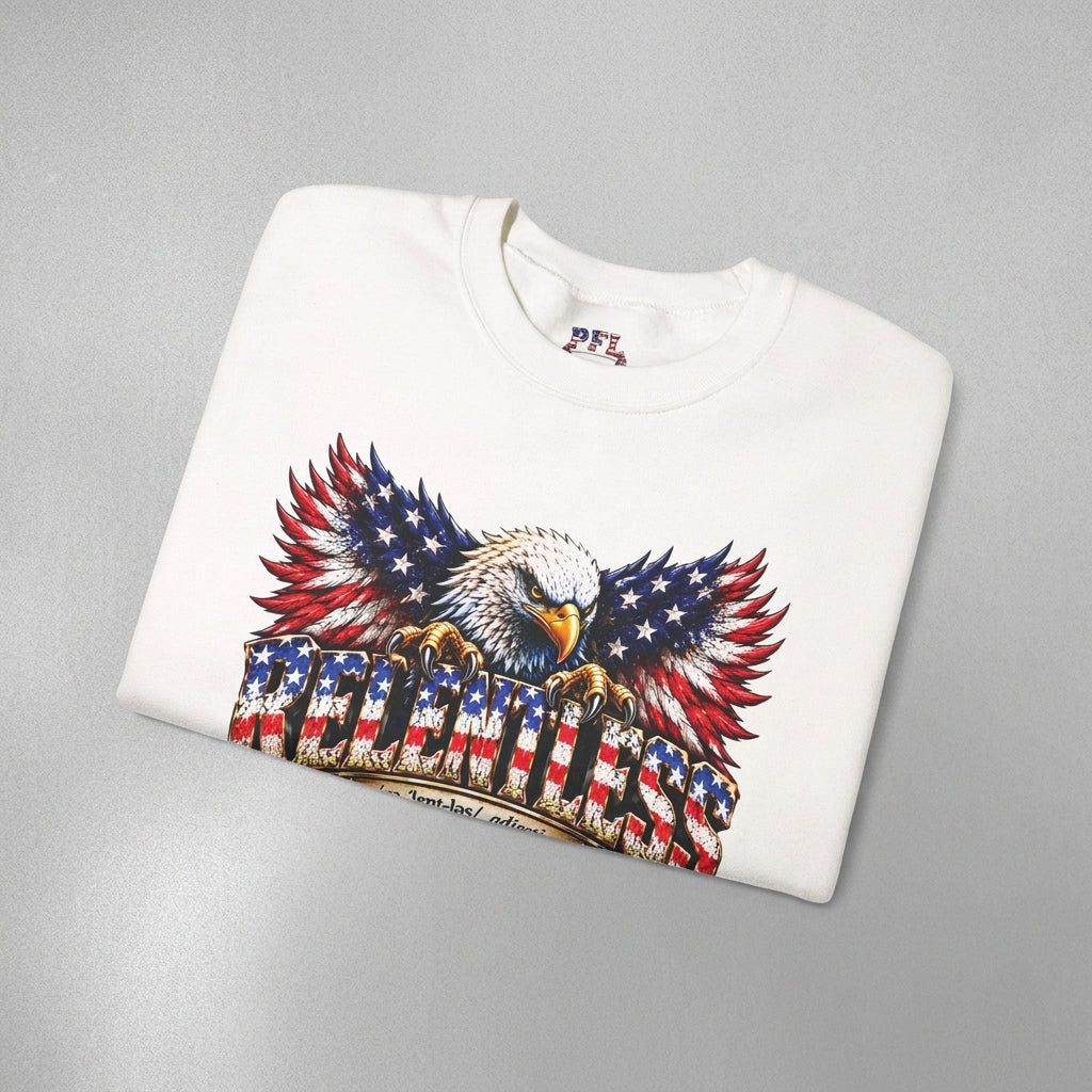 A folded white crewneck sweatshirt featuring a large graphic print of a bald eagle with wings patterned like the American flag, perched on a dictionary-style definition banner that reads RELENTLESS.