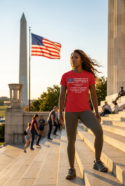 A woman stands on outdoor stone steps in front of the Washington Monument, wearing a bright red UNSTOPPABLE text graphic T-shirt and gray leggings. An American flag is visible in the background, along with other people and the monument.