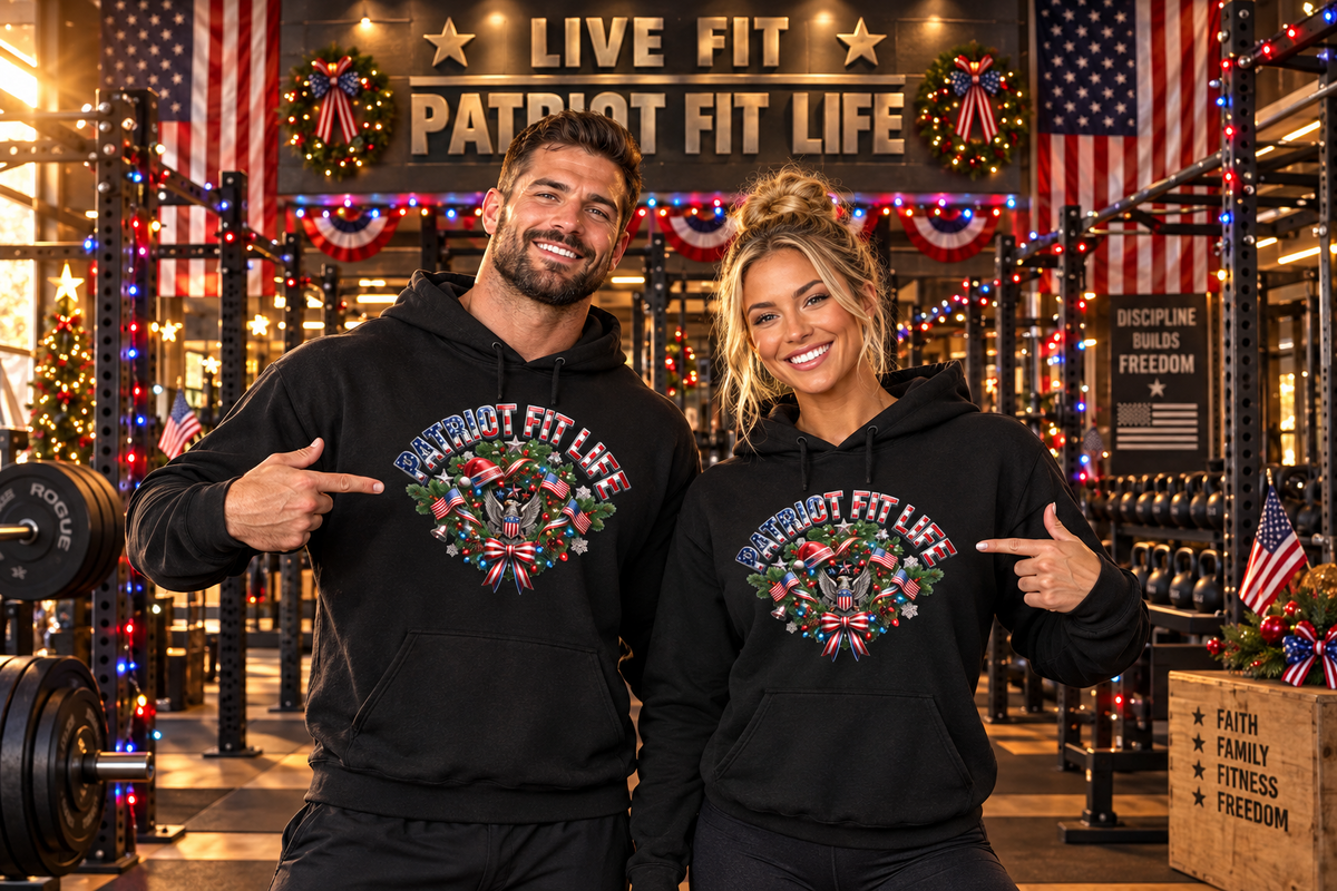 A man and a woman standing in a festive-decorated gym wearing matching black hoodies with a colorful patriotic Christmas-themed graphic that reads 'PATRIOT FIT LIFE'.