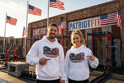 A man and a woman stand in a gym wearing matching white hoodies with a patriotic PATRIOT FIT LIFE American flag graphic on the front. The background features a brick wall with 'PATRIOT FIT' and 'LIVE FIT' signage, along with multiple American flags.