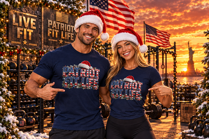 A man and a woman wearing matching navy blue t-shirts with a festive 'Patriot Fit Life' holiday graphic, posing together in front of a snowy outdoor gym at sunset with American flags and the Statue of Liberty in the background.