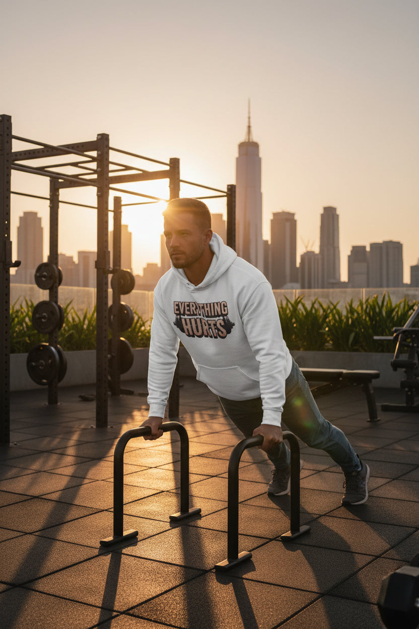 A man wearing a hoodie that says, Everything Hurts, exercising on parallel bars with a city skyline in the background.
