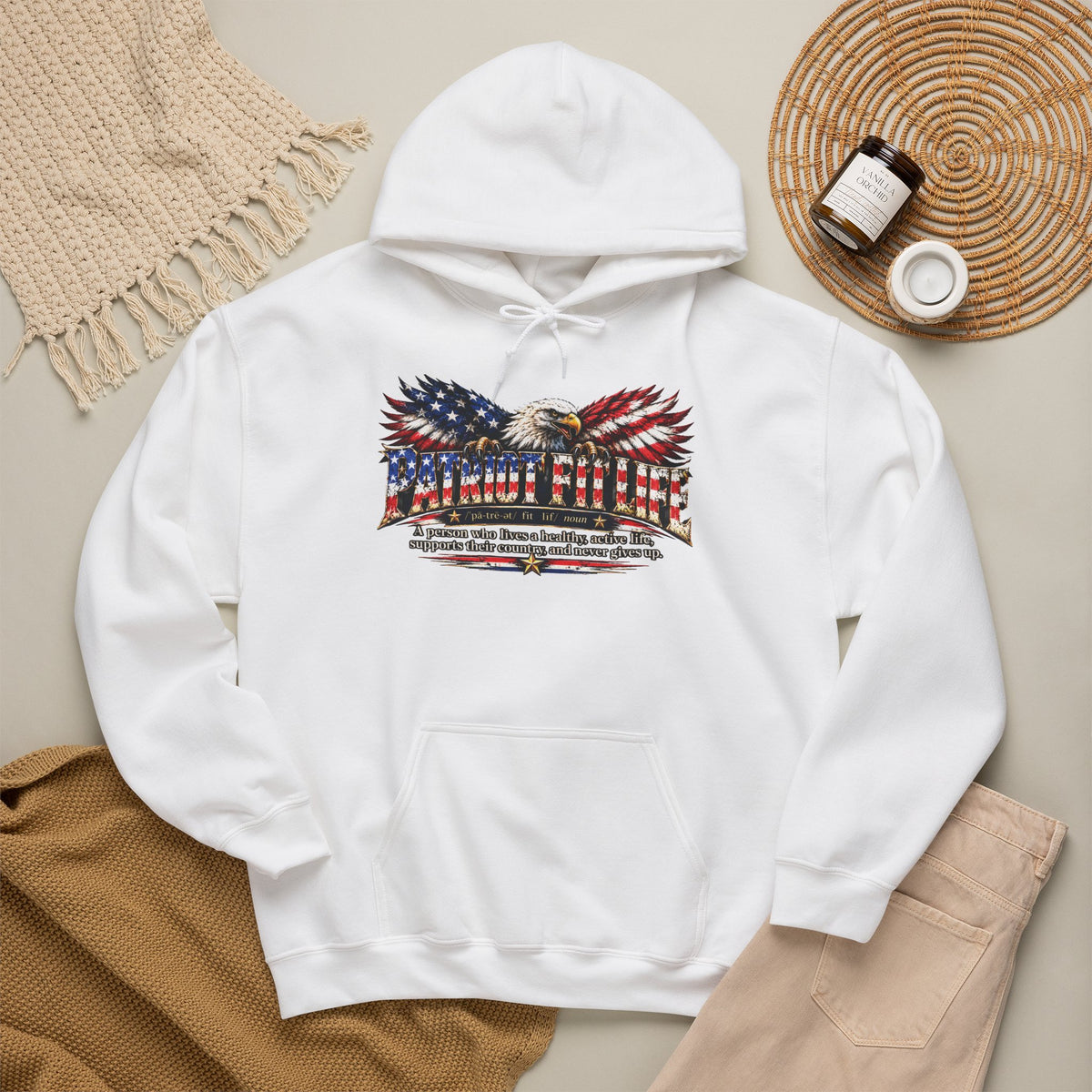 A white pullover hoodie laid flat on a neutral beige surface, featuring a large front PATRIOT FIT LIFE eagle American flag dictionary-style definition graphic. 