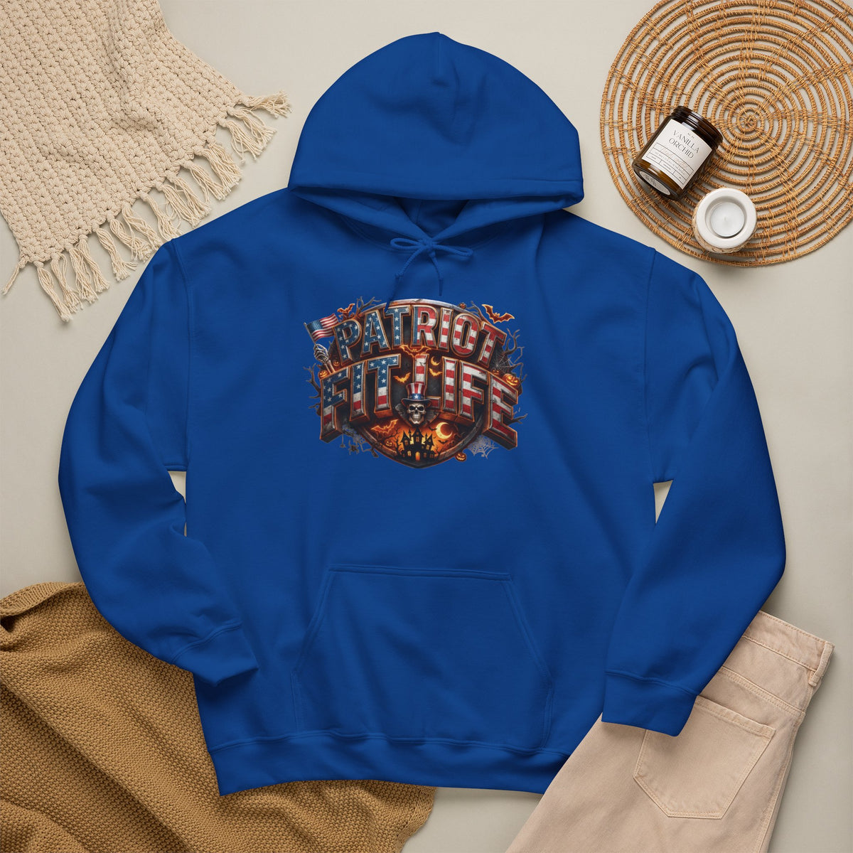 A royal blue pullover hoodie laid flat on a light beige surface, featuring a Halloween graphic design that reads PATRIOT FIT LIFE. 