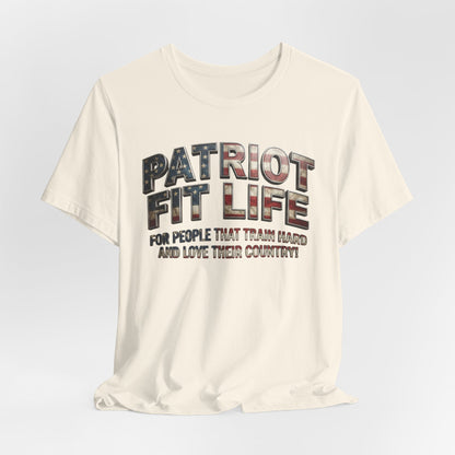 An off-white crewneck t-shirt with a graphic print reading 'PATRIOT FIT LIFE' in a distressed American flag pattern, with the slogan 'FOR PEOPLE THAT TRAIN HARD AND LOVE THEIR COUNTRY!' underneath, shown on a light gray gradient background.