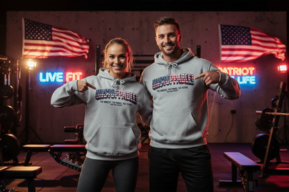 A man and a woman standing in an indoor gym wearing matching light gray hoodies with a patriotic graphic that reads 'UNSTOPPABLE.' Both are pointing toward the chest print.